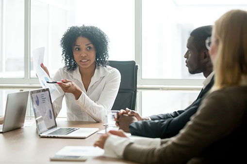 Woman Pointing Out Information on a Document to Colleagues Around a Table