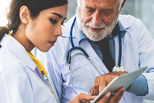 An Older Male Doctor Points Out Something on the Clipboard of a Younger Doctor