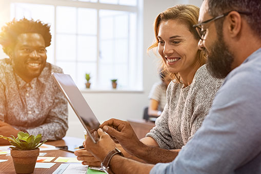 Three Meeting Participants Smiling and Looking at Something on a Tablet