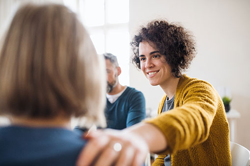 Meeting Participants Around a Table With a Focus on a Single Woman with a Reassuring Hand on a Colleague's Shoulder