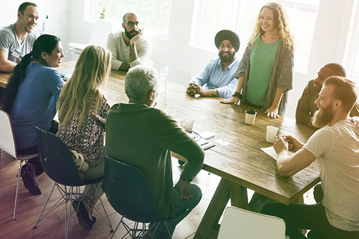 A Group of Colleagues Around a Wooden Meeting Table, With One Woman Standing